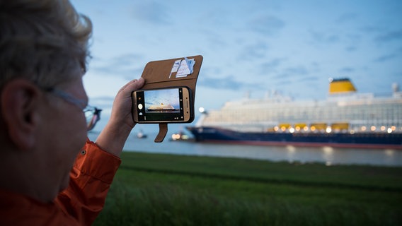Eine Person fotografiert das Kreuzfahrtschiff "Spirit of Discovery", während seiner Überfahrt am frühen Morgen über die Ems. © dpa-Bildfunk Foto: Moritz Frankenberg