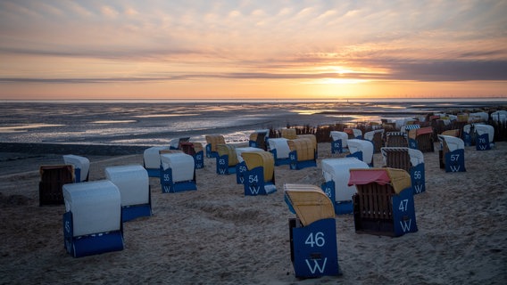 Strandkörbe stehen bei Sonnenaufgang an einem Strand. © dpa-Bildfunk Foto: Sina Schuldt
