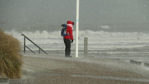 Eine Frau steht an der stürmischen Nordsee im Hagel. © dpa Foto: Volker Bartels