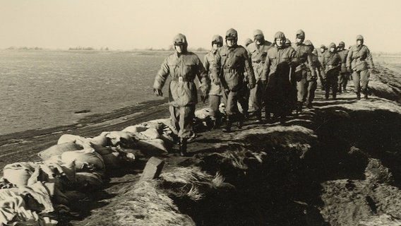 Uniformierte Männer marschieren über den Deich bei Augustgroden am Tag nach der Sturmflut 1962. © Archiv des Rüstringer Heimatbundes e.V. 