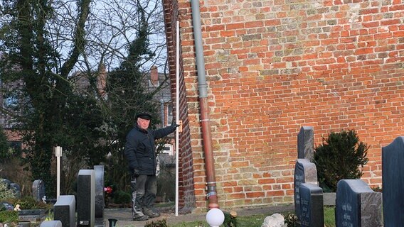 Ein Mann hält einen langen Stab an den Kirchturm von Suurhusen. © NDR Foto: Oliver Gressieker