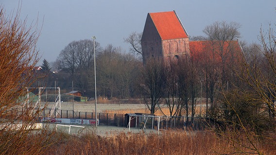 Die schiefe Kirche von Suurhusen hinter einem Sportplatz. © NDR Foto: Oliver Gressieker
