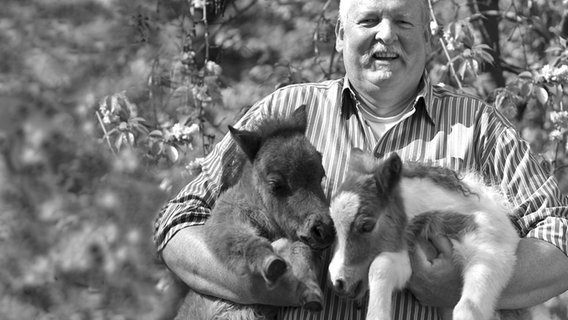 Ein Schwarzweiß-Foto zeigt den 2016 verstorbenen Tamme Hanken mit zwei Fohlen im Arm. © NDR/Miramedia GmbH Foto: Bernd Eilers