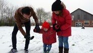 Ein Elternpaar geht mit einem Kleinkind im Schnee spazieren. © NDR Foto: Nadia Yaqub