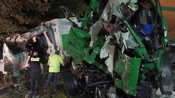 Ein Polizist und ein weiterer Mann stehen vor zwei Lkw-Wracks. © TelenewsNetwork 