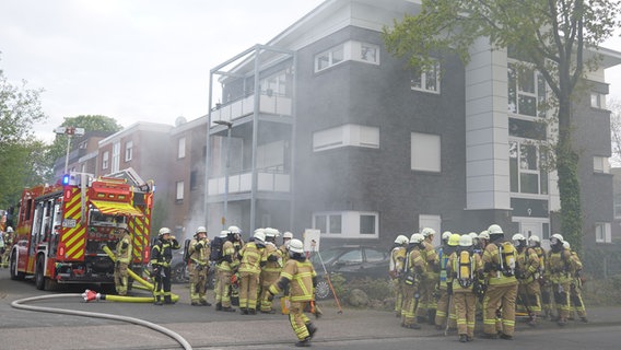 Mehrere Feuerwehrleute stehen vor einem Mehrfamilienhaus in Vechta. Rauch steigt aus dem Gebäude auf. © Nord-West-Media TV 
