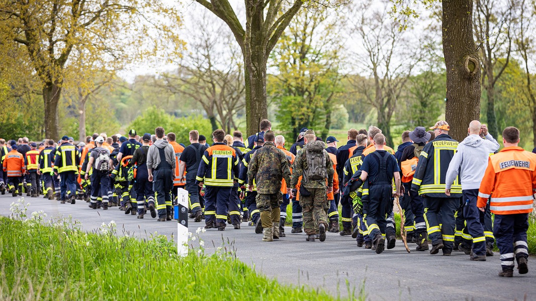 Einsatzkräfte der Feuerwehr und Soldaten der Bundeswehr gehen bei der Suche nach einem vermissten Jungen aus Bremervörde auf einer Straße im Landkreis Stade entlang. 
