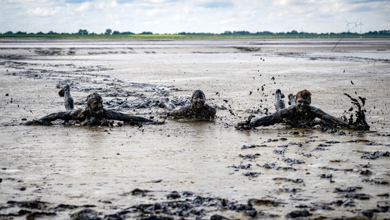 Besucher rutschen beim Watt en Schlick Festival durch das Watt am Strand von Dangast. © dpa Foto: Sina Schuldt