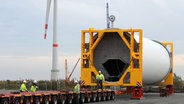 Mitarbeiter der Transportfirma arbeiten vor dem Turmsegment einer Windkraftanlage auf dem Geländer der Firma Cuxhaven Steel Construction GmbH in Cuxhaven am Hänger, der das Segment transportieren soll. © dpa-Bildfunk Foto: Carmen Jaspersen