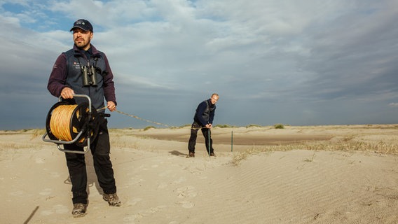 Zwei Nationalpark-Ranger bauen einen mobilen Zaun am Strand auf (für den Strandbrüter-Schutz auf Borkum). © Lukas Lehmann Foto: Lukas Lehmann