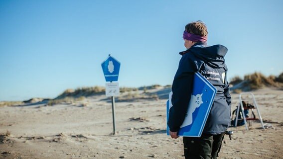 Eine Nationalpark-Rangerin hält ein blaues Schild unter dem Arm (Beschildern der Schutzzonen auf Baltrum). © Lukas Lehmann Foto: Lukas Lehmann