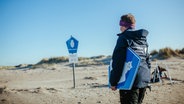Eine Nationalpark-Rangerin hält ein blaues Schild unter dem Arm (Beschildern der Schutzzonen auf Baltrum). © Lukas Lehmann Foto: Lukas Lehmann