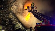 Ein Feuerwehrmann auf einer Drehleiter löscht ein brennendes Haus in Worpswede. © NonstopNews 