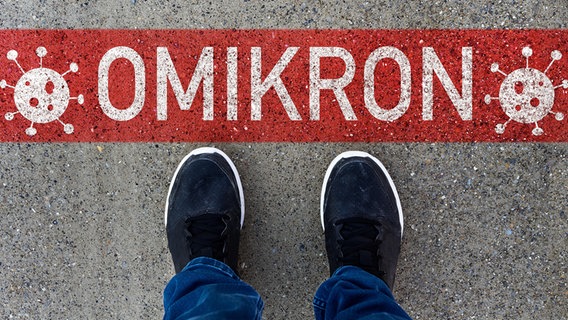 Ein Mann steht vor einem Schriftzug "Omikron" auf einer Straße.  © CHROMORANGE Foto: Michael Bihlmayer