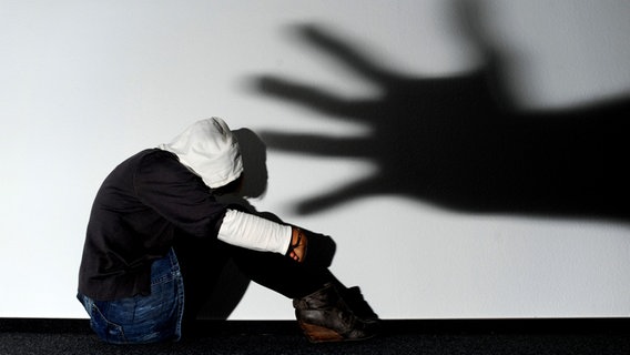Ein Mädchen sitzt vor einer Wand, auf der der Schatten einer Hand groß zu sehen ist. © dpa-Bildfunk Foto: Julian Stratenschulte