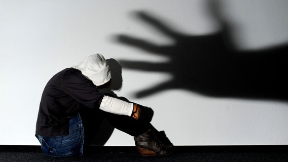 Ein Mädchen sitzt vor einer Wand, auf der der Schatten einer Hand groß zu sehen ist. Ein Mädchen sitzt vor einer Wand, auf der der Schatten einer Hand groß zu sehen ist. © dpa-Bildfunk Foto: Julian Stratenschulte