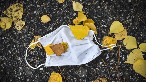 Eine getragene OP-Maske liegt auf dem Boden zwischen Herbstlaub. © picture alliance / Bildagentur-online/Ohde Foto: Ohde