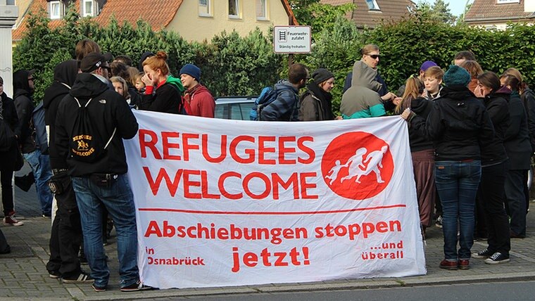 Eine Menschengruppe steht auf einer Straße und hält ein Transparant mit der Aufschrift "Refugees Welcome". © NDR Fotograf: Jörg Holzapfel