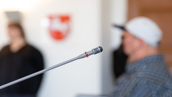 Ein Tischmikrofon ist vor einem Angeklagten in einem Saal vom Amtsgericht zu sehen. © dpa-Bildfunk Foto: Friso Gentsch/dpa