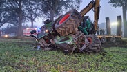 Ein umgekippter Traktor liegt nach einem Unfall mit einem Pkw in einem Acker neben einer Straße. © Nord-West-Media TV 