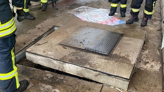 Einsatzkräfte der Feuerwehr stehen in einer Tankstelle in der Bergstraße in Bissendorf um eine Betonplatte herum, nachdem dort ein Blitz eingeschlagen ist. Der Blitzeinschlag führte zu einer Explosion in einem stillgelegten Öltank wodurch die Betonlpatte hochgeschleudert wurde. Ein Autofahrer wurde dabei leicht verletzt. © Polizei Osnabrück 