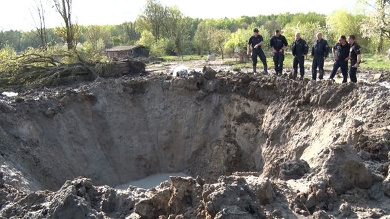 Einsatzkräfte des Kampfmittelräumdients stehen an einem Krater. © Nord-West-Media TV 