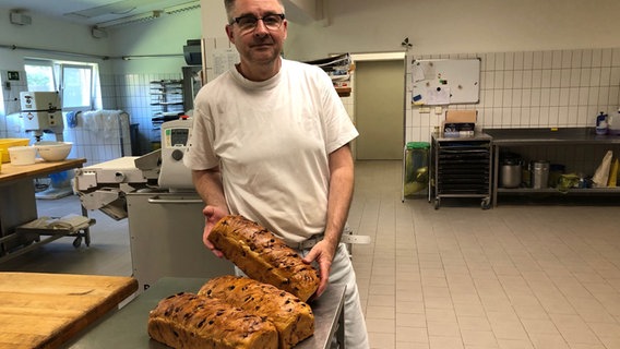 Ein Mann präsentiert Brotlaibe in einer Backstube. © NDR Foto: Hewdig Ahrens