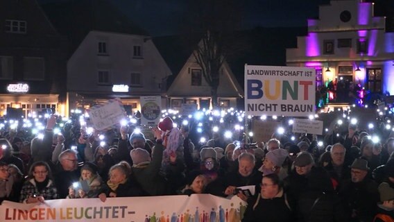 Bei einer Demo in Lingen halten Teilnehmende leuchtende Smartphones und Plakate in die Luft. © TV7news 