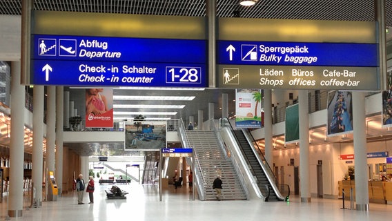 Flughafenhalle mit Treppe und Rolltreppe. Schilder zum Check-in-Schalter und zur Abflugzone. © NDR Foto: Carsten Ehrbar