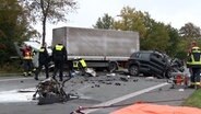 Einsatzkräfte von Polizei und Feuerwehr stehen an einer Unfallstelle auf der B214 in Fürstenau, nachdem ein Auto frontal mit einem Lkw zusammengestoßen ist. Bei dem Unfall kamen die Fahrer beider Fahrezuge ums Leben. © Nord-West-Media TV 