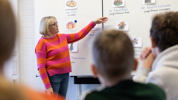 Lehrerin Hilde Uffelmann steht im Unterricht in einer Sprachlernklasse mit ukrainischen Schülern an der Tafel. Davor Schüler. © Friso Gentsch/dpa Foto: Friso Gentsch/dpa