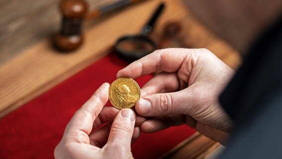 Ein Mann hält bei einer Auktion eine alte russische Goldmünze in der Hand. © dpa-Bildfunk/Auktionshaus Künker 