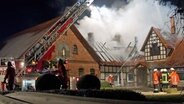 Ein Löschfahrzeug mit Kran und mehrere Feuerwehrleute stehen vor einem brennenden Gutshaus auf einem Bauernhof in Hagen am Teutoburger Wald. © dpa-Bildfunk Foto: Friso Gentsch