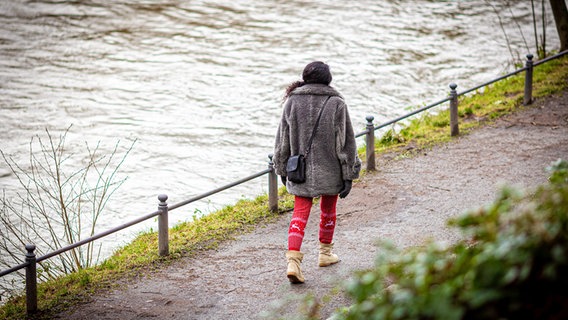 Eine Frau geht bei trübem Wetter in Osnabrück am Herrenteichswall am Fluss Hase, der Hochwasser führt, spazieren. © dpa Foto: Moritz Frankenberg