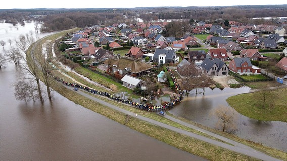 Einsatzkräfte und Einwohner sichern mit einer Menschenkette gemeinsam einen durchweichten Deich im Landkreis Emsland. © dpa-Bildfunk 