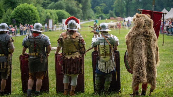 Darsteller in Kostümen der Römischen Legion "Ferrata" stehen am Rande der Arena der Römer und Germanentage. © dpa Foto: Lino Mirgeler