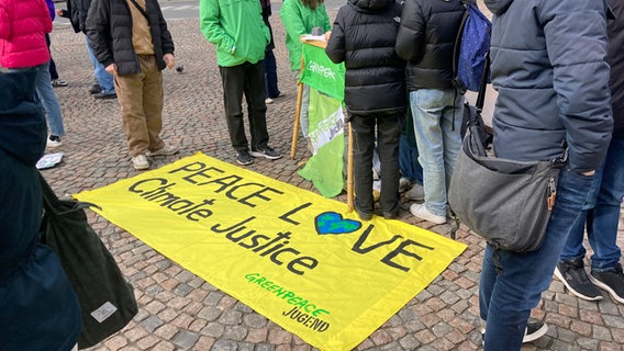 Auf einer Demonstration von "Fridays for Future" liegt ein Transparent auf dem Boden mit der Aufschrift: "Peace, Love, Climate Justice". © NDR Foto: Andreas Gervelmeyer