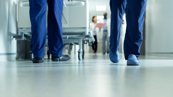 Mitarbeitende laufen über einen Gang im Krankenhaus © picture alliance / Zoonar 