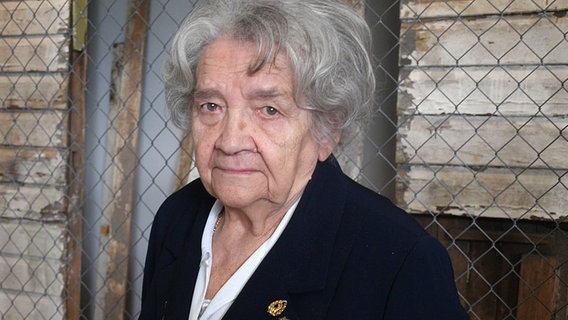 Eine ältere Frau mit grauem Haar steht vor einem Stacheldrahtzaun. © NDR Foto: Hedwig Ahrens