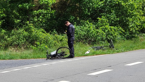 Ein Polizist steht neben zwei Fahrrädern, die nach einem Unfall am Straßenrand liegen. © Nord-West-Media TV 