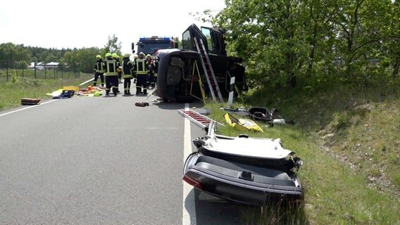 Zwei Feuerwehrleute stehen neben einem Autowrack ohne Dach nach der Bergung des  verunglückten Fahrers. © Nord-West-Media TV 