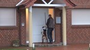 Ein Polizist mit einem Suchhund vor einem Wohnhaus in Lingen © Nord-West-Media TV 