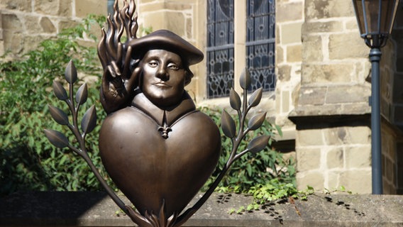 Eine Bronze-Figur von Martin Luther steht vor einer Kirchenmauer. © NDR Foto: Josephine Lüttke