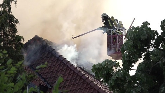 Ein Feuerwehrmann auf einer Drehleiter vor einem brennenden Haus in Melle © Nord-West-Media TV 