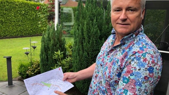 Ein Mann steht in seinem Garten und zeigt eine Karte. © NDR Foto: Hedwig Ahrens