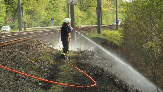 Ein Feuerwehrman löscht einen Vegetationsbrand, der wegen heißgelaufener Räder eines Güterzuges entstanden ist. © Nord-West-Media TV 