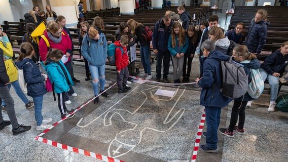 Ministranten blicken bei einem Krimi-Rätselspiel auf den Boden der Herz-Jesu-Kirche. © dpa-Bildfunk Foto: Friso Gentsch