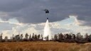 Ein Hubschrauber lässt Wasser aus einem Löschwasser-Außenlastbehälter auf die Moorlandschaft nieder. © Bundeswehr 