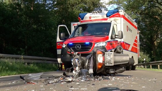Ein Roller liegt nach einem Unfall in Neuenkirchen auf der Straße, im Hintergrund ein Rettungswagen. © Nord-West-Media-TV 