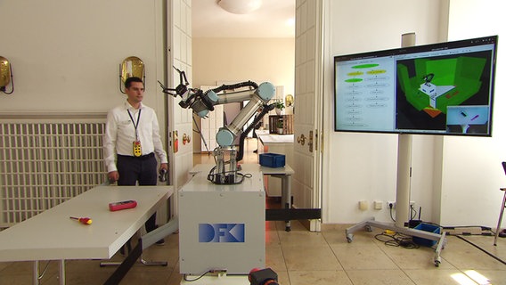 Ein Mann steht neben einem Roboter-Arm. © NDR 